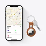 ردیاب اپل AirTag قرارگرفته در جاسوئیچی چرمی قهوه‌ای در کنار صفحه ردیابی کلیدها روی آیفون